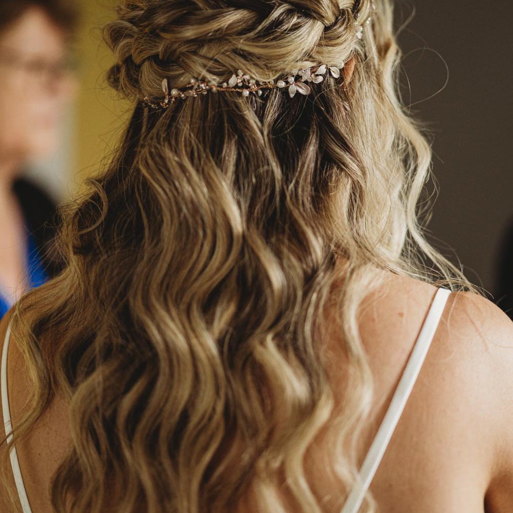 Bridal half-up style with a braided crown, soft waves and a delicate hair vine, styled by Tilly