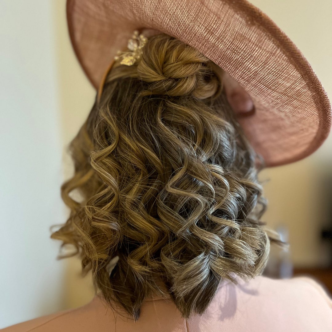 Occasion style with a twisted top knot and defined curls under a rose coloured hat